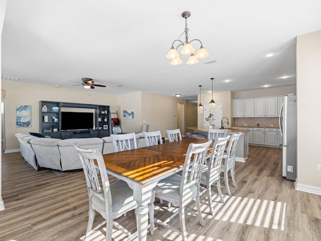 dining space featuring light hardwood / wood-style floors, sink, and ceiling fan with notable chandelier