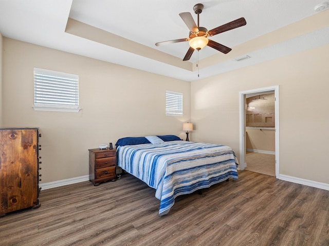 bedroom with ceiling fan, dark wood-type flooring, ensuite bathroom, and a raised ceiling