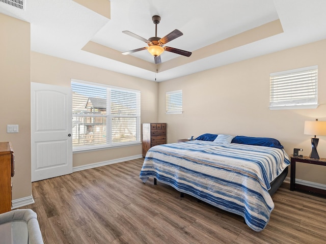 bedroom featuring ceiling fan, a tray ceiling, and dark wood-type flooring