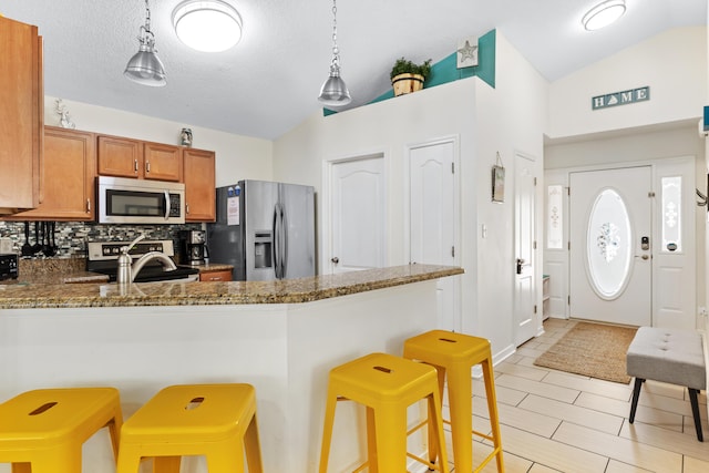 kitchen featuring backsplash, hanging light fixtures, vaulted ceiling, appliances with stainless steel finishes, and a breakfast bar area