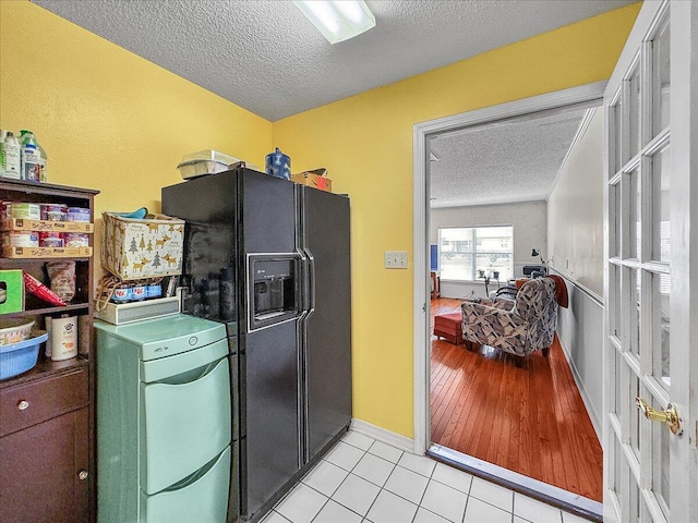 kitchen with black fridge with ice dispenser, light tile patterned floors, and a textured ceiling