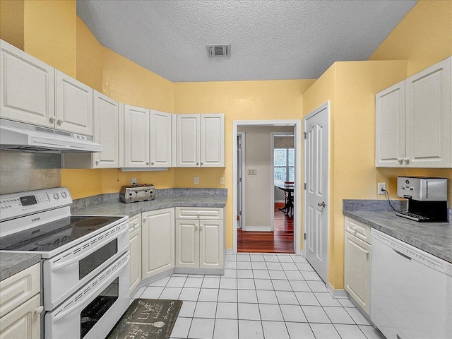 kitchen featuring a textured ceiling, light tile patterned floors, white cabinets, and white appliances