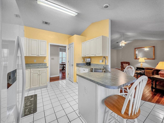 kitchen with lofted ceiling, sink, white cabinets, and white refrigerator with ice dispenser