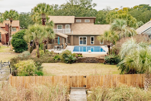 rear view of property featuring a balcony, fence private yard, a lawn, and a fenced in pool