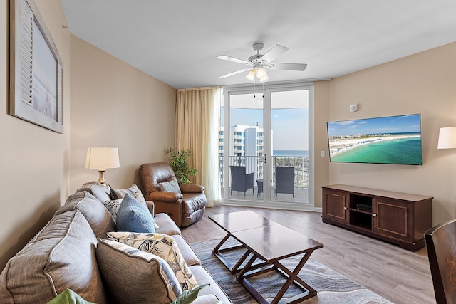 living room with a wall of windows, ceiling fan, and light wood-type flooring