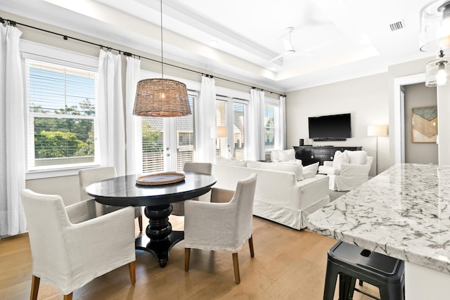 dining room featuring light wood-type flooring, a tray ceiling, and plenty of natural light