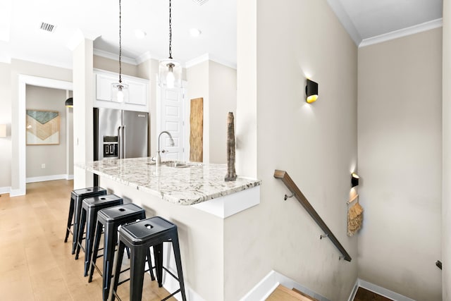 kitchen featuring pendant lighting, a kitchen bar, sink, high end fridge, and white cabinetry