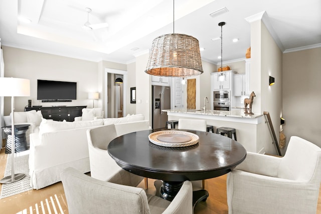 dining space featuring light wood-type flooring, a tray ceiling, ornamental molding, ceiling fan, and sink