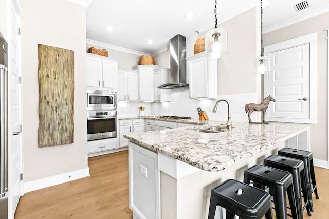 kitchen with stainless steel appliances, white cabinets, kitchen peninsula, wall chimney range hood, and a breakfast bar