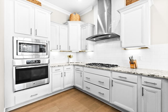 kitchen with stainless steel appliances, white cabinets, ornamental molding, and wall chimney exhaust hood