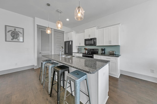 kitchen featuring black appliances, decorative light fixtures, a center island with sink, and white cabinets