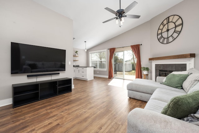 living room with a tiled fireplace, wood-type flooring, high vaulted ceiling, and ceiling fan