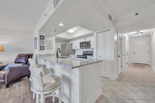 kitchen with kitchen peninsula, light stone countertops, stainless steel appliances, a breakfast bar area, and white cabinetry