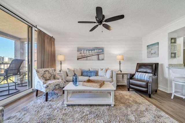 living room with a textured ceiling, ceiling fan, hardwood / wood-style flooring, and ornamental molding