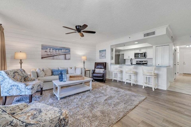 living room with a textured ceiling, ceiling fan, wood walls, and wood-type flooring