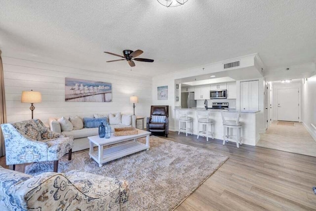 living room with a textured ceiling, ceiling fan, light hardwood / wood-style flooring, and wooden walls