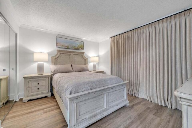 bedroom featuring a closet, a textured ceiling, ornamental molding, and light hardwood / wood-style floors