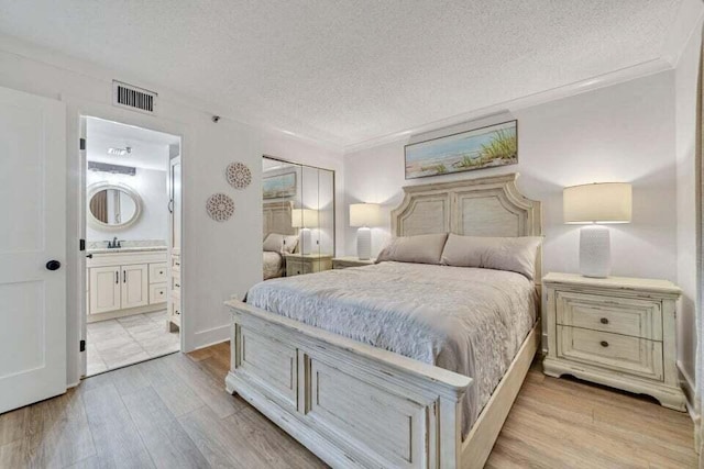 bedroom featuring ensuite bathroom, a textured ceiling, light hardwood / wood-style flooring, and sink