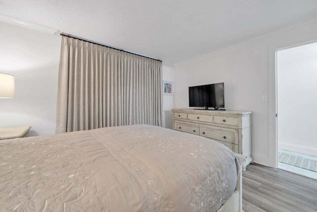 bedroom with a textured ceiling, crown molding, and light hardwood / wood-style flooring