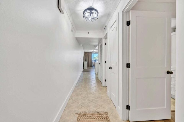 hallway with a textured ceiling, light tile patterned flooring, and crown molding