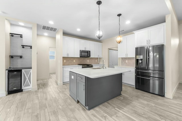 kitchen with appliances with stainless steel finishes, white cabinets, sink, and a center island with sink