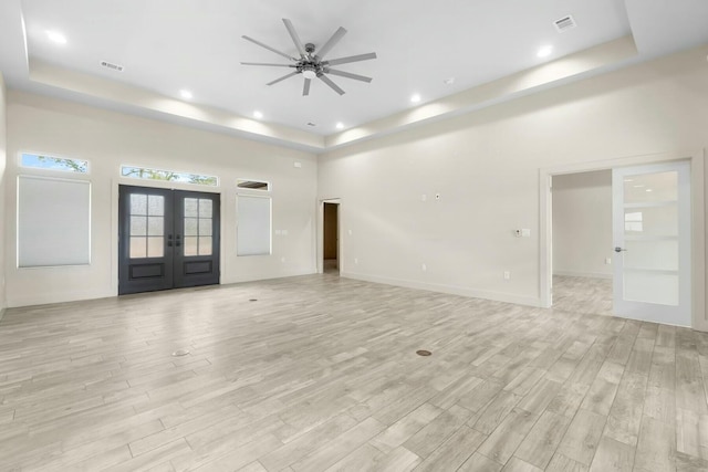 unfurnished living room featuring french doors, a raised ceiling, ceiling fan, and light hardwood / wood-style flooring