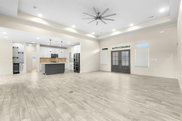 unfurnished living room featuring french doors, ceiling fan, a tray ceiling, and light hardwood / wood-style flooring