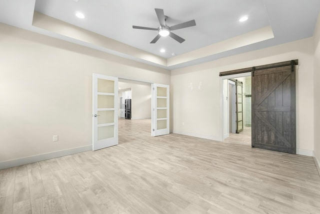 spare room with french doors, ceiling fan, a tray ceiling, and a barn door