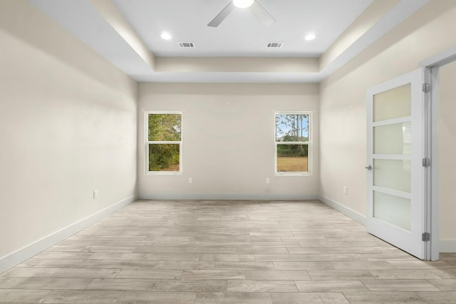 empty room featuring ceiling fan, light hardwood / wood-style flooring, plenty of natural light, and a tray ceiling