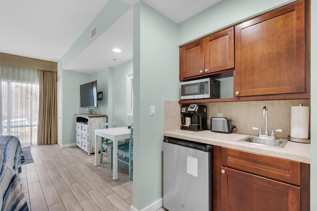 kitchen with decorative backsplash, refrigerator, light hardwood / wood-style floors, and sink