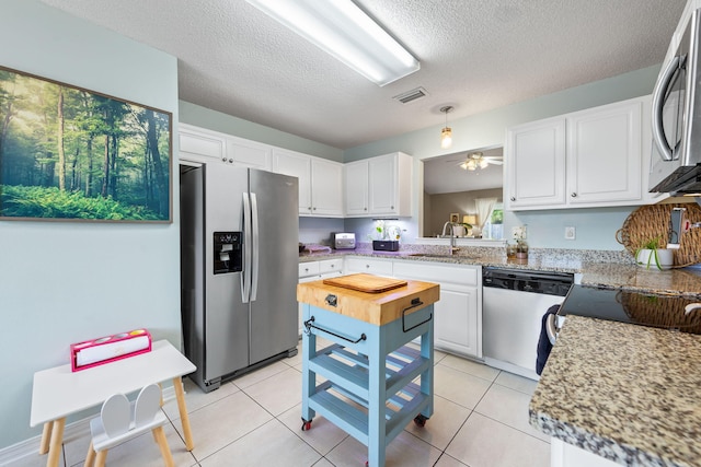 kitchen featuring ceiling fan, a textured ceiling, light tile patterned floors, white cabinets, and stainless steel appliances