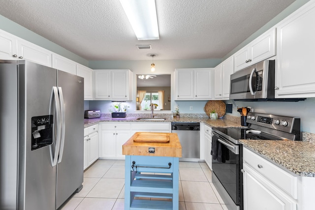 kitchen with a center island, appliances with stainless steel finishes, white cabinetry, sink, and light tile patterned flooring