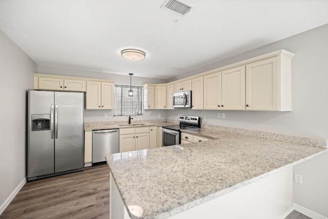 kitchen with appliances with stainless steel finishes, pendant lighting, sink, kitchen peninsula, and cream cabinetry