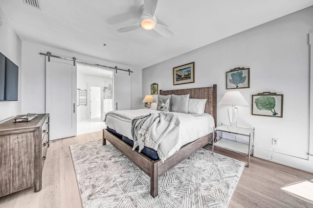 bedroom with ceiling fan, a barn door, ensuite bathroom, and light hardwood / wood-style flooring