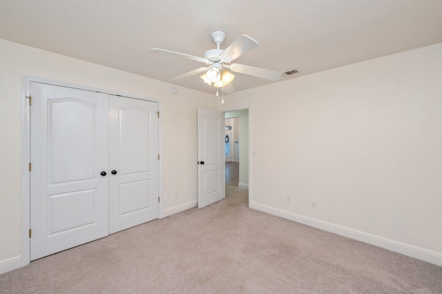 unfurnished bedroom with ceiling fan, light colored carpet, a textured ceiling, and a closet