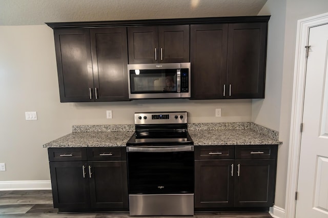 kitchen with stainless steel appliances, light stone countertops, and dark brown cabinets