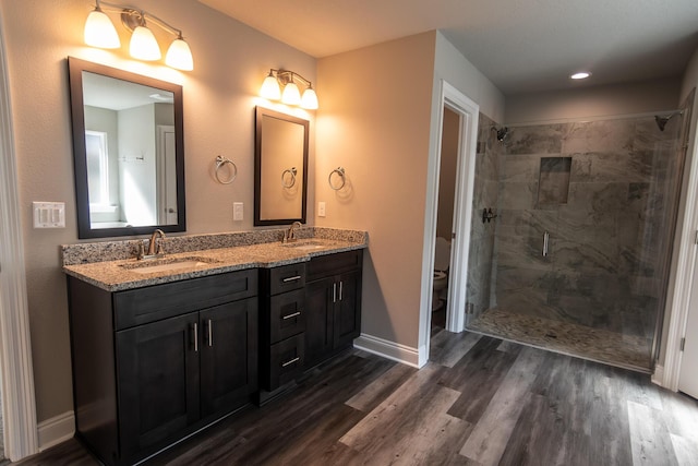 bathroom featuring wood-type flooring, toilet, vanity, and a tile shower