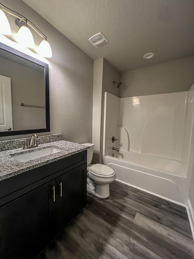 full bathroom with wood-type flooring, vanity, toilet, bathing tub / shower combination, and a textured ceiling