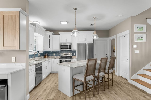 kitchen with appliances with stainless steel finishes, a kitchen island, sink, white cabinetry, and decorative light fixtures