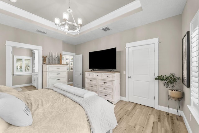 bedroom with a notable chandelier, light wood-type flooring, and a tray ceiling