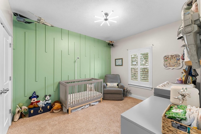 bedroom with a nursery area, a textured ceiling, and carpet floors