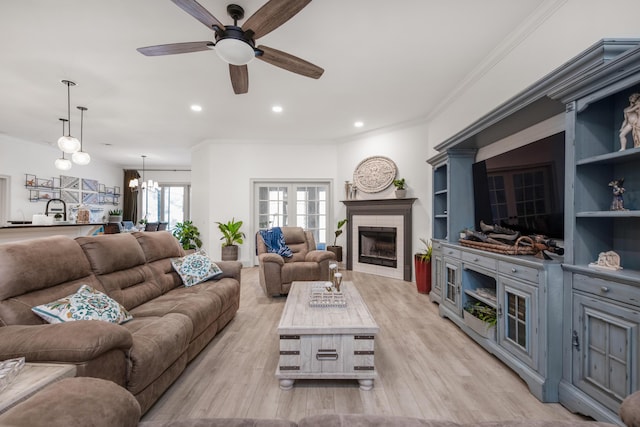 living room featuring light wood-style flooring, ornamental molding, ceiling fan with notable chandelier, recessed lighting, and a brick fireplace