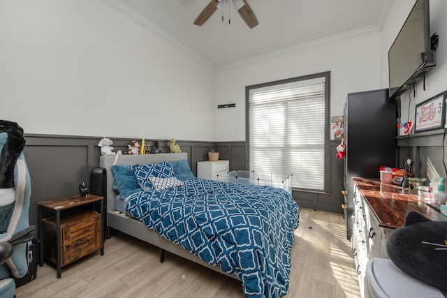 bedroom with ceiling fan, light wood-style flooring, wainscoting, and crown molding