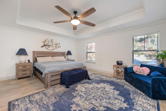 bedroom with a raised ceiling, crown molding, wood finished floors, and baseboards