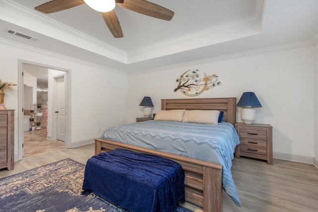 bedroom with a ceiling fan, visible vents, light wood finished floors, crown molding, and a raised ceiling