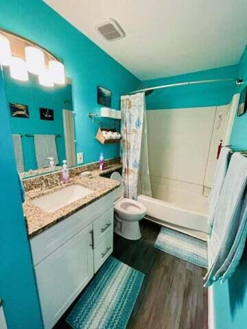 full bathroom with toilet, shower / bathtub combination with curtain, hardwood / wood-style floors, and vanity