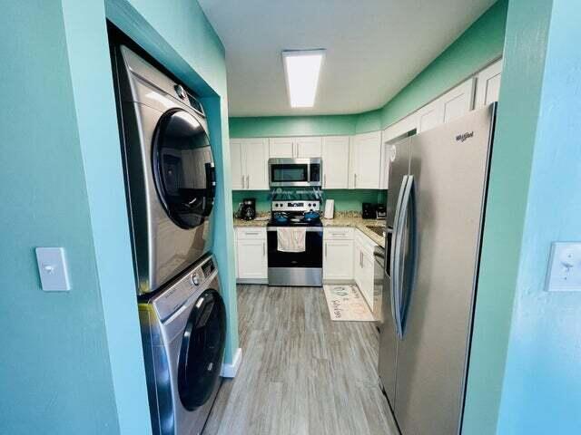 kitchen featuring stacked washer and dryer, stainless steel appliances, white cabinets, and light wood-type flooring