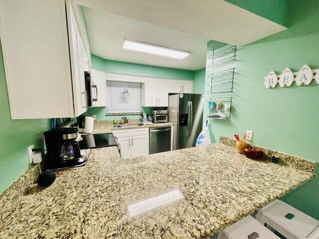 kitchen featuring white cabinets, kitchen peninsula, appliances with stainless steel finishes, and light stone counters