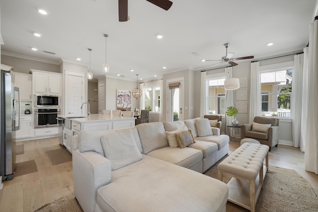 living room featuring ceiling fan, sink, ornamental molding, and light hardwood / wood-style flooring