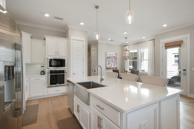 kitchen with white cabinets, appliances with stainless steel finishes, decorative light fixtures, sink, and a center island with sink